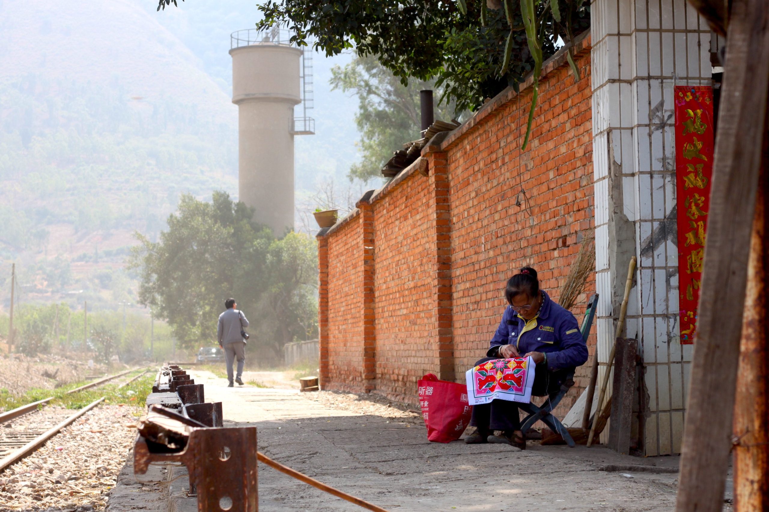 A local villager works on a piece of colorful embroidery near the former Xialongtan Train station that was built in the early 1900's by the French when constructing the Yunnan-Vietnam Railway