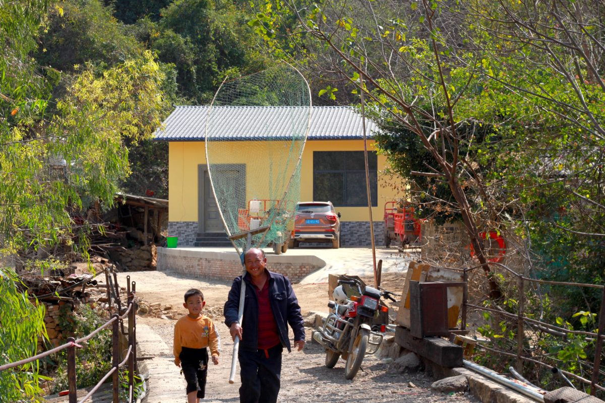 A Miao minority villager walks with a small boy while holding a large fishing net in Xiaolongtan Village and Flower Bridge, Honghe Prefecture