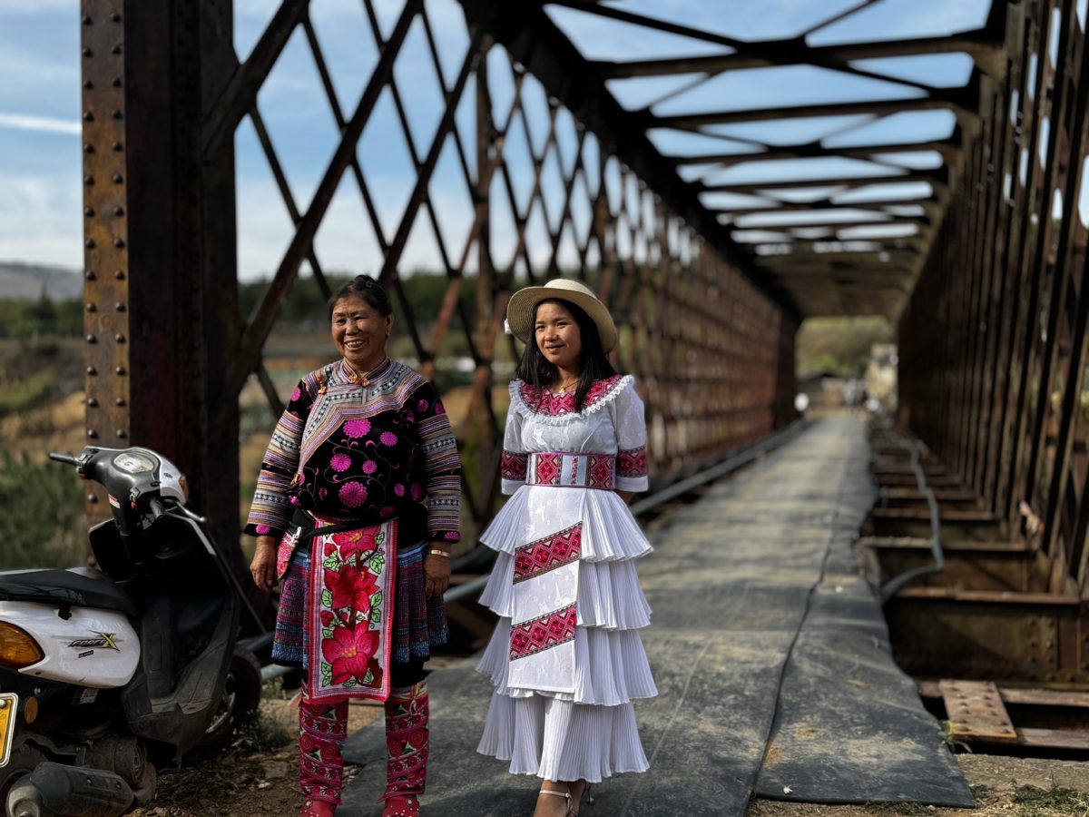 Miao minority villagers show their ethnic minority apparel with Xiaolongtan's Flower Bridge behind them